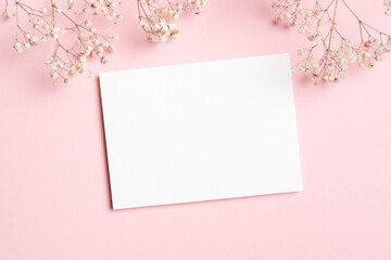 Horizontal white blank card mockup decorated with baby breath flowers on a pastel pink background, perfect for wedding invitations or greeting cards, flat lay