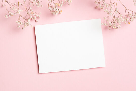 Horizontal white blank card mockup decorated with baby breath flowers on a pastel pink background, perfect for wedding invitations or greeting cards, flat lay - Powered by Adobe