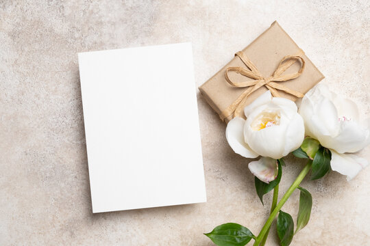 Blank wedding invitation mockup with copy space, elegant peony flowers and gift box, perfect for personalized greeting card designs and special occasion announcements
