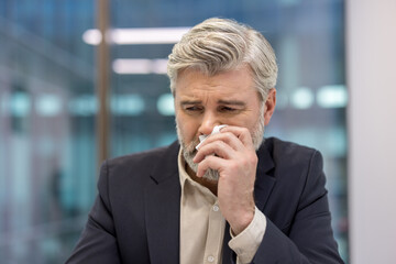 Mature businessman experiencing emotional distress or sadness, wiping tears with a tissue, conveying concepts of grief, stress, loss, anxiety, and vulnerability in a corporate setting