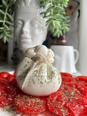 buratta cheese with sliced tomatoes and Provencal herbs on the background of a flower pot in the...