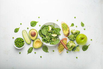 Fresh green salad bowl, avocado toasts, raw vegetables fruit white concrete background top view, diet, vegetarian food. Set of different green healthy products, clean eating nutrition