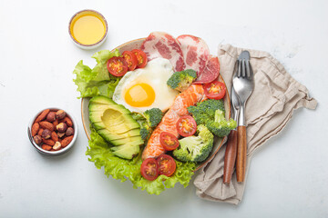 Healthy ketogenic diet concept showing a balanced meal on plate with salmon, avocado, fried egg, bacon, broccoli, tomato, and fresh salad, promoting low carb and high fat eating