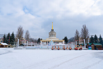 Beautiful wide shot of the central VDNKh (Expocenter of Ukraine) pavilion in Kyiv on a snowy winter day, showing the decorated ice rink