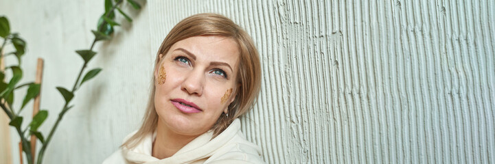 Naklejka premium Caucasian female adult with cosmetic face treatment relaxing against textured wall in a spa environment.