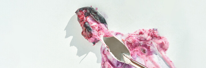Melting berry ice cream on white background with metal ice cream scoop revealing texture.