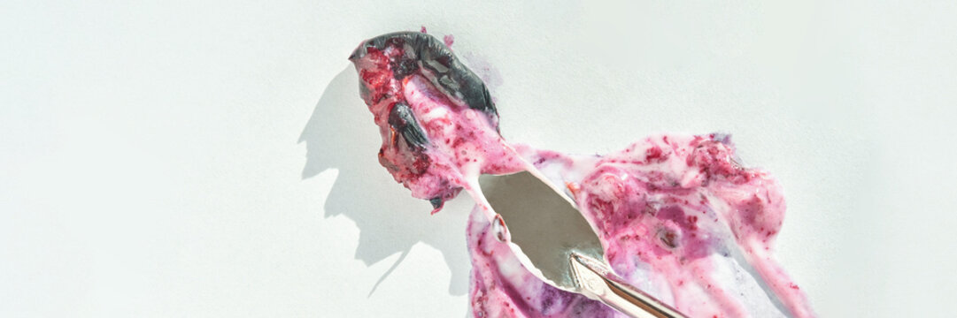 Melting berry ice cream on white background with metal ice cream scoop revealing texture.