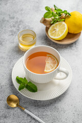 Tea with lemon, ginger, honey, and mint in a cup on a gray background with citrus fruits