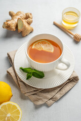 Hot tea with lemon, ginger, honey, and mint in a cup on a light background with citrus fruits