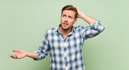 Confused man scratching head expression portrait with green background