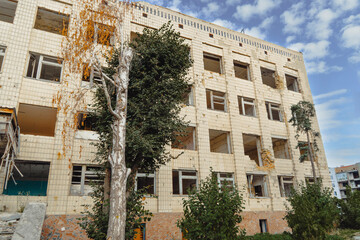 Low-angle view of a multi-story residential building severely damaged by war, showing numerous destroyed windows, exposed interiors, and a peeling facade