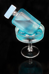 Blue bottle of eau de toilette in a cocktail glass with blue ice on a dark background