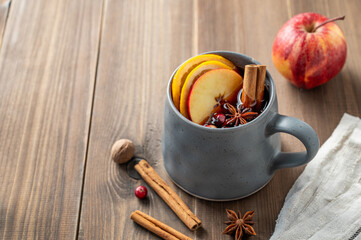 A cup of red mulled wine with spices, orange, apple slices and cranberry on a wooden background