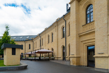 Charming outdoor cafe terrace with light-colored umbrellas against the restored facade of a historic yellow-brick building on a cloudy summer day