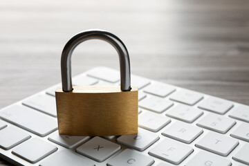 Password concept. Closed padlock and keyboard on wooden table, closeup
