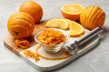 Orange zest, fresh fruits and zester tool on light grey table, closeup