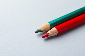 Red and green eye pencils on light background, closeup. Space for text