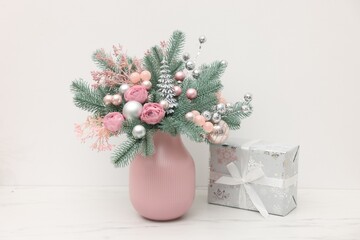 Beautiful composition with fir tree branches in vase and gift box on light marble table near white wall indoors. Winter decor