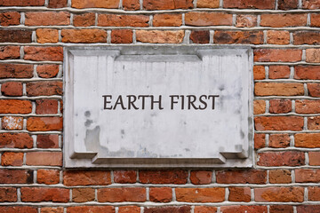 A weathered stone plaque with the words Earth First stands prominently on a textured brick wall, reflecting an emphasis on environmental protection and sustainability in urban landscapes