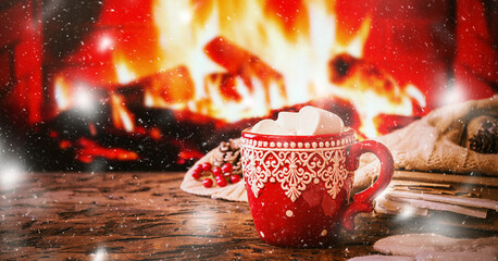 Mug of hot chocolate or coffee with marshmallows in a red mug on vintage wood table in front of Fireplace as a background. Christmas or winter warming drink.