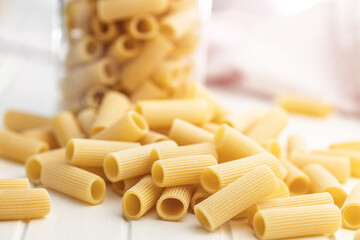 Uncooked rigatoni pasta on white table.