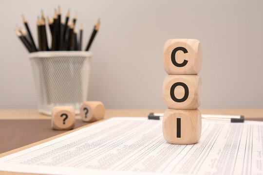 Wooden cubes stacked vertically forming word COI on financial table with pencils in background
