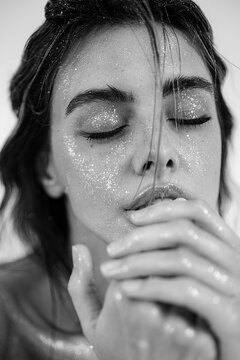 Studio close-up of a beautiful woman with natural makeup, wet hair, and sparkling glitter on her skin. 