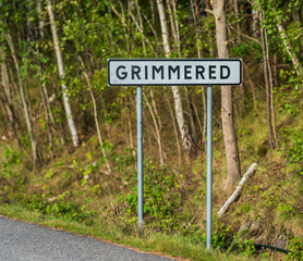 Town sign Grimpered with forest background.