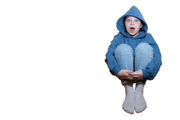 A child with a shocked or scared expression sits hugging his knees, wearing a blue hoodie and jeans on a transparent background with space for text.