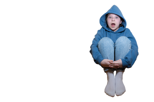 A child with a shocked or scared expression sits hugging his knees, wearing a blue hoodie and jeans on a transparent background with space for text.