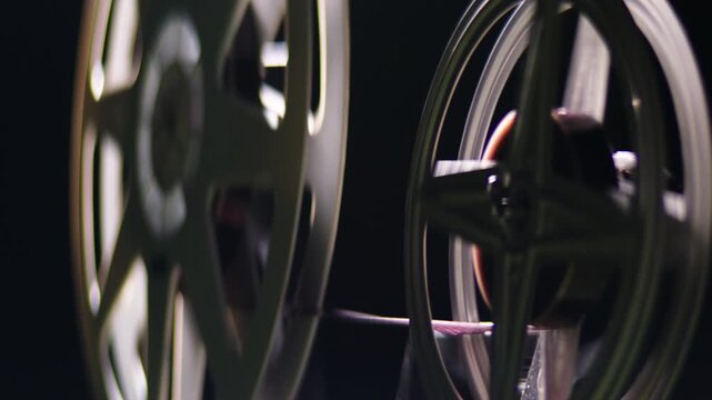 Close-up of a retro film reel spinning as tape unwinds from the spool on a professional projector, illustrating the classic process of moviemaking, cinema exhibition, and archival footage