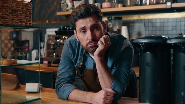 Disappointed Caucasian waiter man barista boredom in cafeteria exhausted employer problem bartender male entrepreneur leaning counter waitstaff overworking cafe guy contemplate small business stress