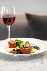 Gourmet plated dish of pork fillet or beef tenderloin with a side of purée, cooked vegetables, and fresh berries, paired with a glass of red wine in a fine dining setting.