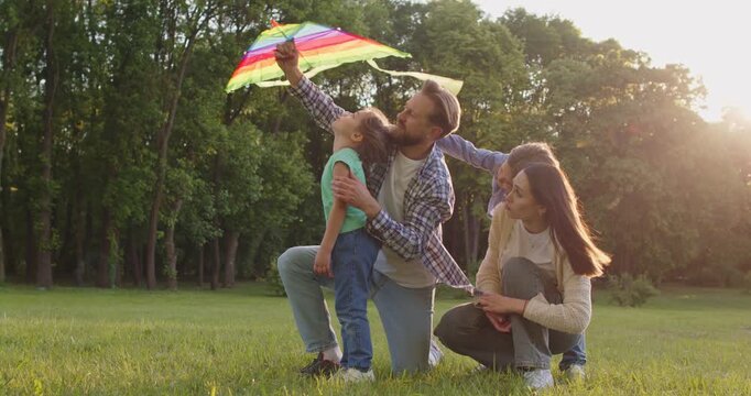 Father, mother and their two children flying kite during windy weather, posing in park, enjoying pastime, enjoying camping trip, spending free time together. Family vacation concept