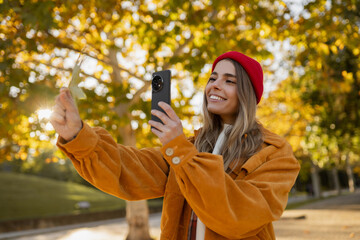 young attractive blond woman walking in autumn park, stylish , smiling, using smartphone