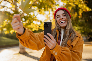 young attractive blond woman walking in autumn park, stylish , smiling, using smartphone
