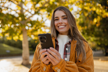young attractive blond woman walking in autumn park, stylish , smiling, using smartphone