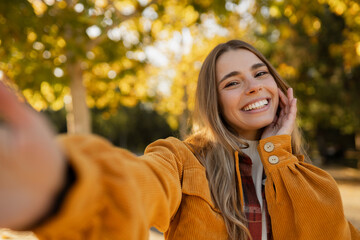 young attractive blond woman walking in autumn park, stylish , smiling, happy mood, taking selfie photo