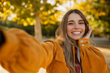 young attractive blond woman walking in autumn park, stylish , smiling, happy mood, taking selfie photo