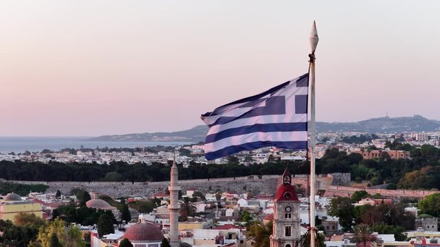 Greece flag waves over rhodes town at dusk offering panoramic views of buildings and aegean sea