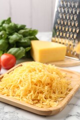 Grated cheese, grater and products on white marble table, closeup