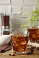 Tasty coffee with ice in glasses and beans on wooden table against light textured background, closeup