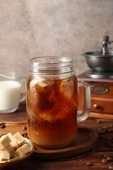 Tasty iced coffee, milk, sugar, grinder and beans on wooden table