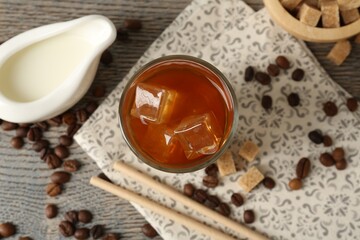 Tasty iced coffee with milk in glass, beans and sugar cubes on wooden table, flat lay