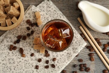 Tasty coffee with ice in glass, beans, milk and sugar cubes on wooden table, flat lay