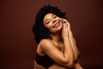 Confident woman smiling against brown backdrop, embracing positivity and diversity, highlighting self-care
