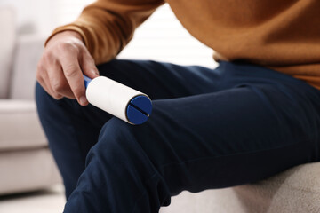 Fototapeta premium Man cleaning pants with lint roller on pouf at home, closeup