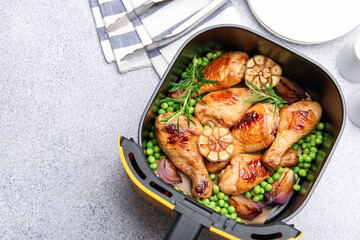 Air fryer basket with grilled chicken drumsticks, spices, green peas and tongs on grey table, flat lay. Space for text