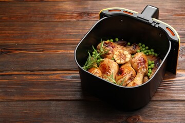 Air fryer basket with grilled chicken drumsticks, spices and green peas on wooden table, closeup. Space for text