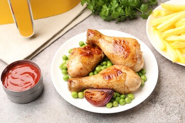 Grilled chicken drumsticks served with green peas and french fries on grey table, above view